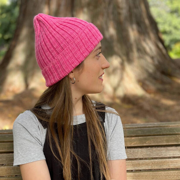 Young women sitting on a bench seat wearing pink hand knitted beanie with raised crown and overalls
