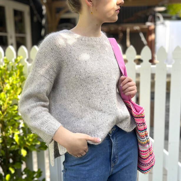 Young women wearing a hand knitted mohair sweater and carrying a bag over her shoulder standing next to picket fence