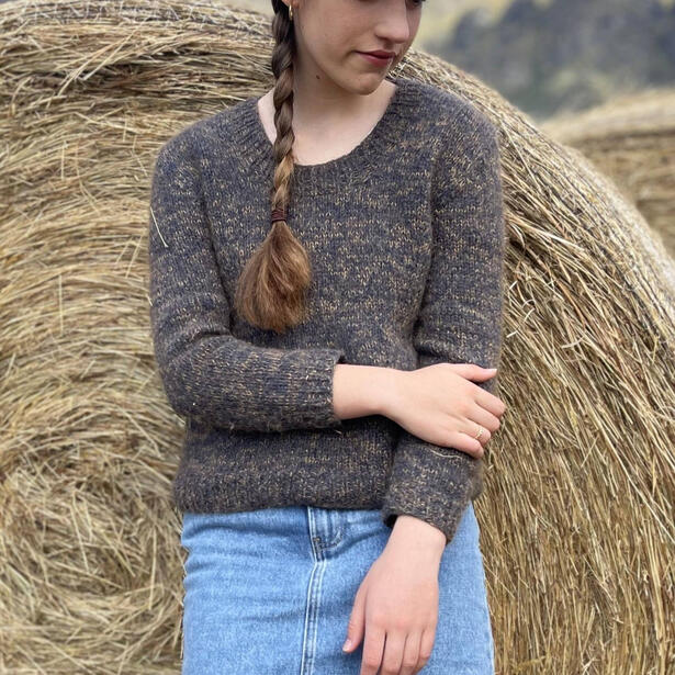 Young women wearing a mohair and wool sweater with marled colour of dark blue and navy standing by a hay bale