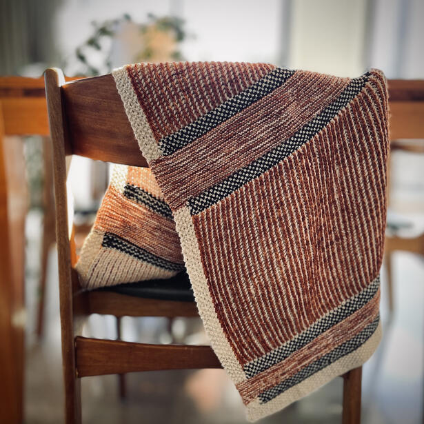 Knitted shawl made of brioche stitch, linen stitch and seed stitch draped over wooden chair