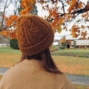 Women wearing a golden brown cable beanie and standing amongst autumn trees