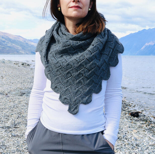 Women standing next to a lake surrounded by mountains wearing a grey-blue shawl with a scalloped edge and white tee