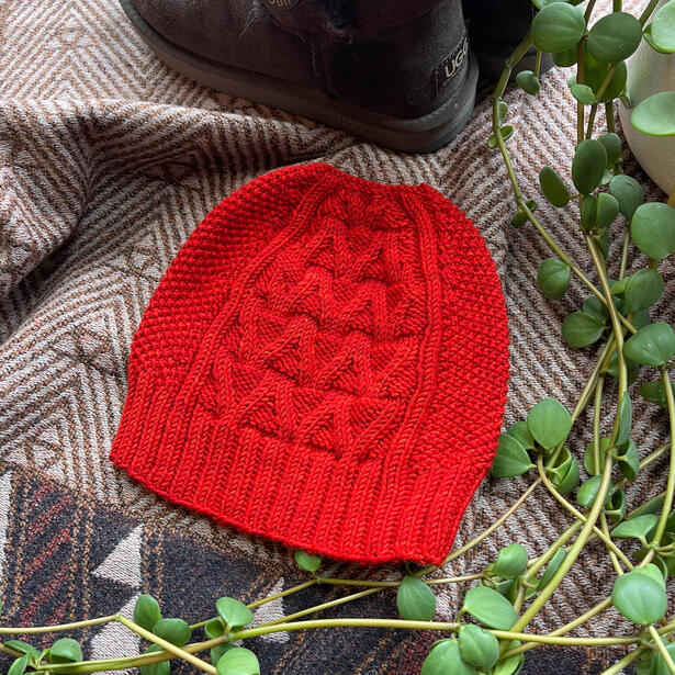 Bright red beanie laid out on a blanket surrounded by warm boots and leaves