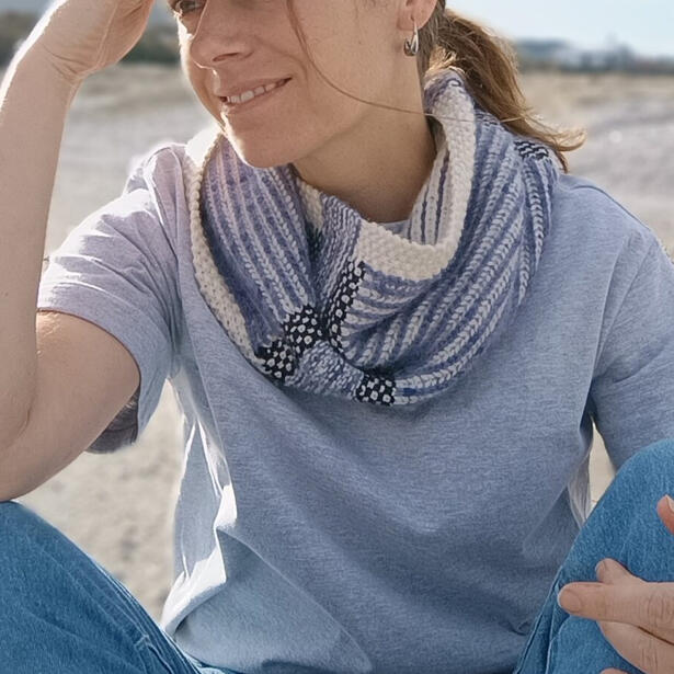Women wearing a cream, blue and charcoal knitted cowl of brioche stitch, linen stitch and seed stitch.