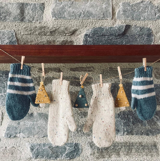 Two pairs of mittens hanging over on a string over a fireplace with Christmas decorations