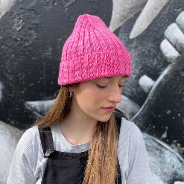Girl wearing a pink hand knitted beanie with a raised crown and overalls