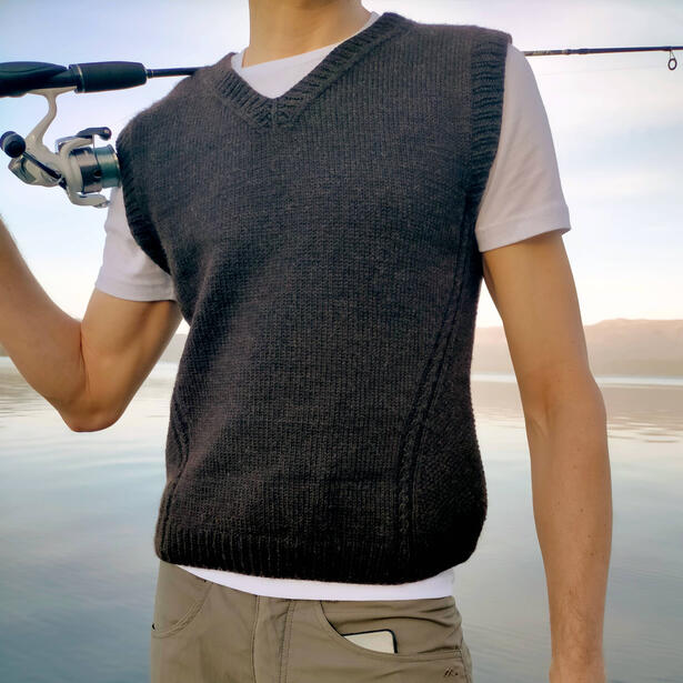 Man wearing a hand knitted vest with seed stitch panels and holding a fishing rod