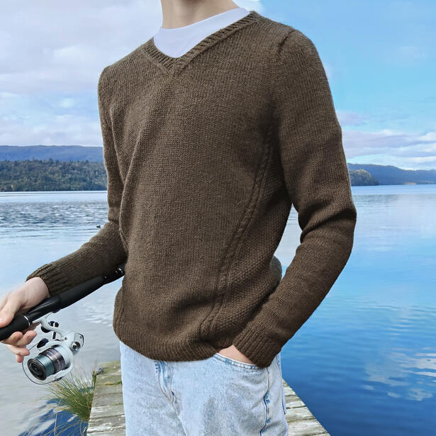 Young Man wearing brown coloured knitted sweater with textured panels and holding a fishing rod