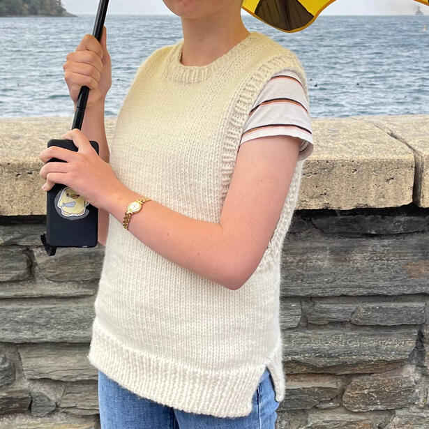 Young women wearing a cream knitted vest and holding an umbrella standing near the waters edge