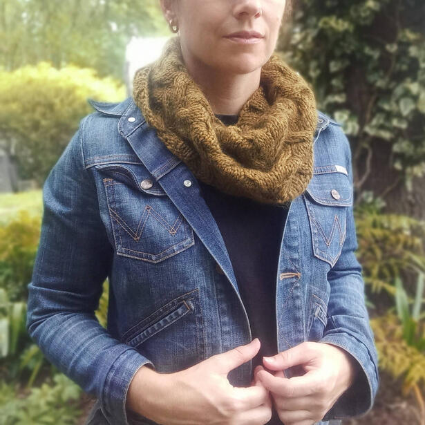 Women wearing an olive green hand knitted cable cowl and denim jacket